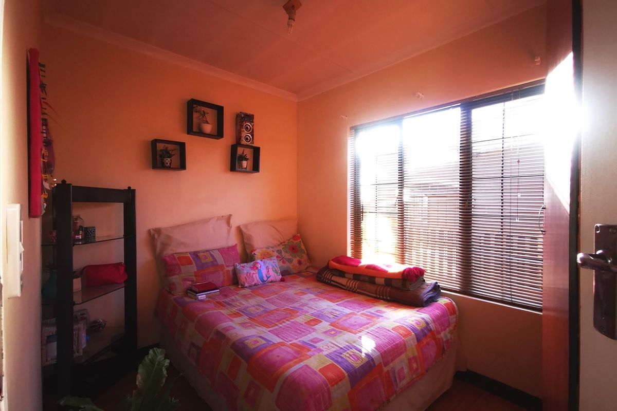 A compact bedroom featuring laminate flooring and venetian blinds, providing natural light and a functional layout.