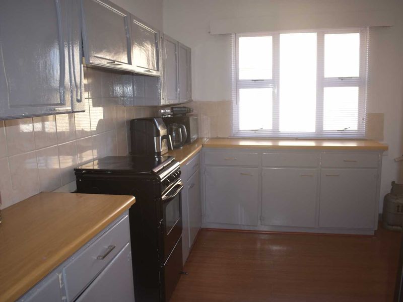 A functional kitchen featuring laminate countertops, tiled backsplash, and painted cabinetry with a freestanding stove.