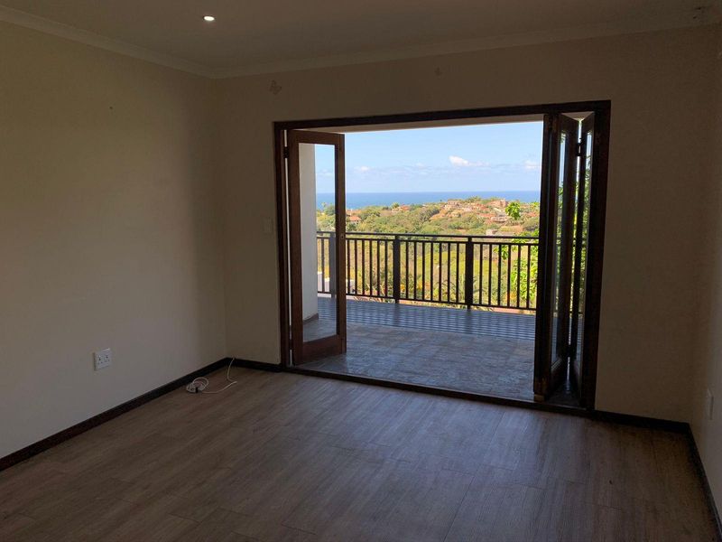 An empty living room featuring laminate flooring, recessed lighting, and wooden folding doors that open onto a balcony with scenic coastal views.