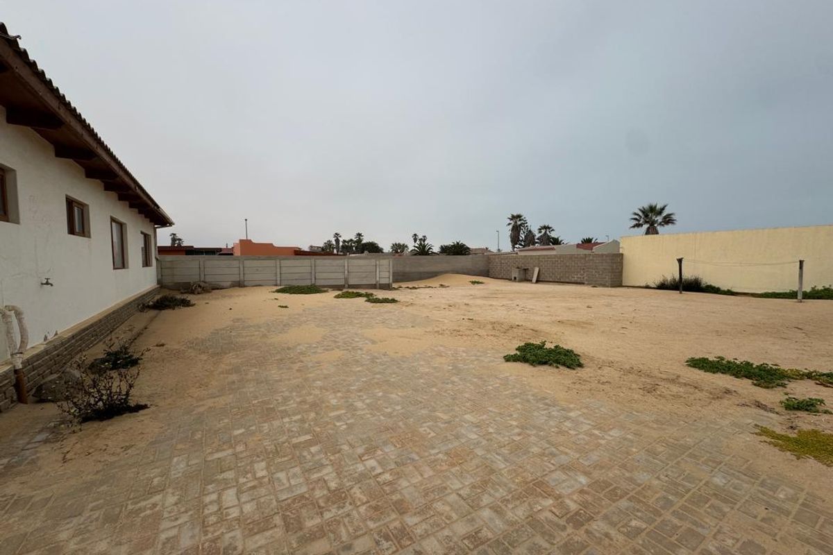 A spacious rear exterior area featuring paved sections, sandy ground, and perimeter boundary walls, offering significant potential for landscaping and outdoor development.