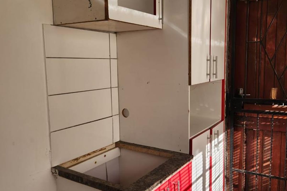 A small kitchen area featuring red and white cabinetry with a granite countertop, currently missing a sink unit.