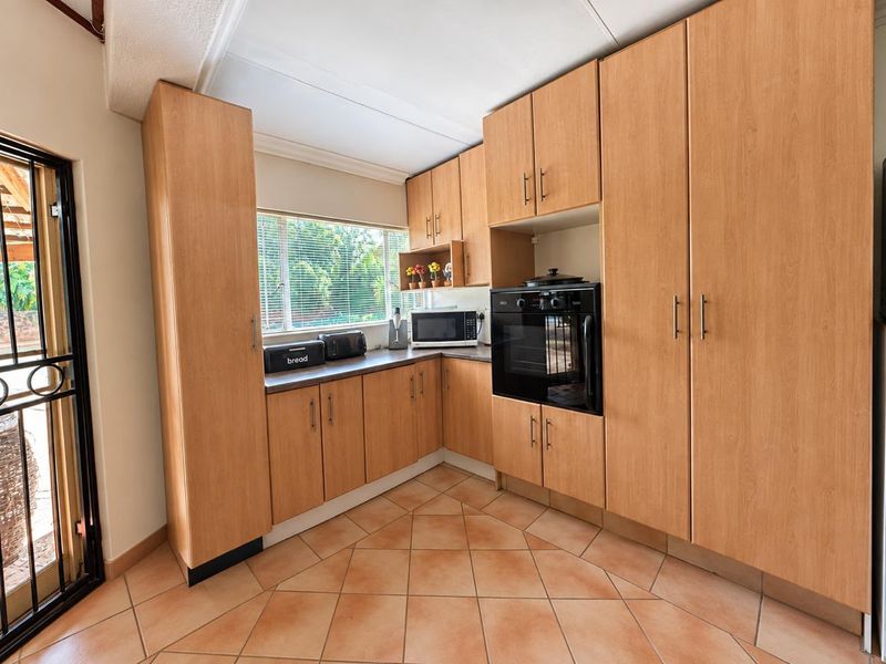 A functional kitchen featuring light wood-finish cabinetry, built-in oven, tiled flooring, and direct access to an outdoor area through a security gate.