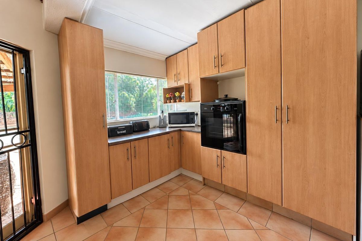 A functional kitchen featuring light wood-finish cabinetry, built-in oven, tiled flooring, and direct access to an outdoor area through a security gate.