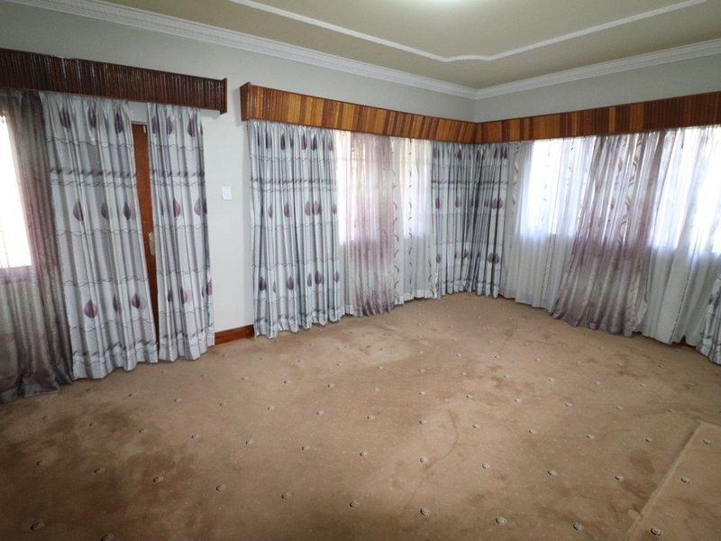 A spacious, empty living room featuring neutral carpet flooring, decorative ceiling cornices, and wooden pelmets above the window treatments.