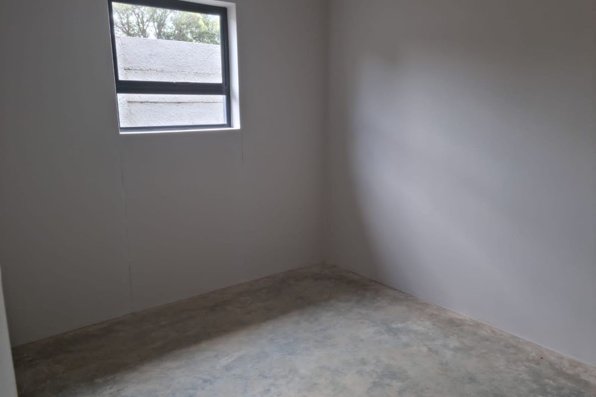 An empty, unfinished bedroom featuring bare concrete flooring and a single window, providing a blank canvas for interior design and flooring installation.