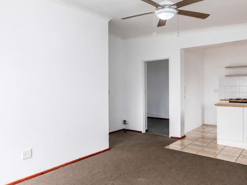 An open-plan living area featuring carpeted flooring, a ceiling fan, and an adjoining kitchen space with tiled flooring and built-in cabinetry.