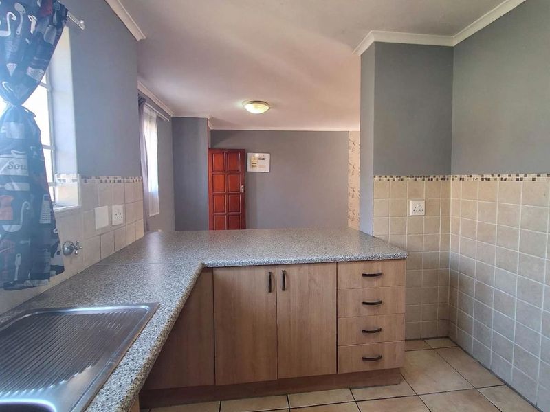 A functional kitchen area featuring laminate cabinetry, granite-look countertops, a stainless steel sink, and neutral ceramic tiling throughout.