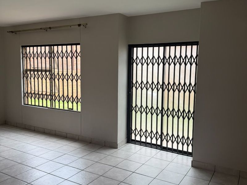 An empty living area featuring neutral tiled flooring, security gates on the sliding door, and window security bars for added safety.