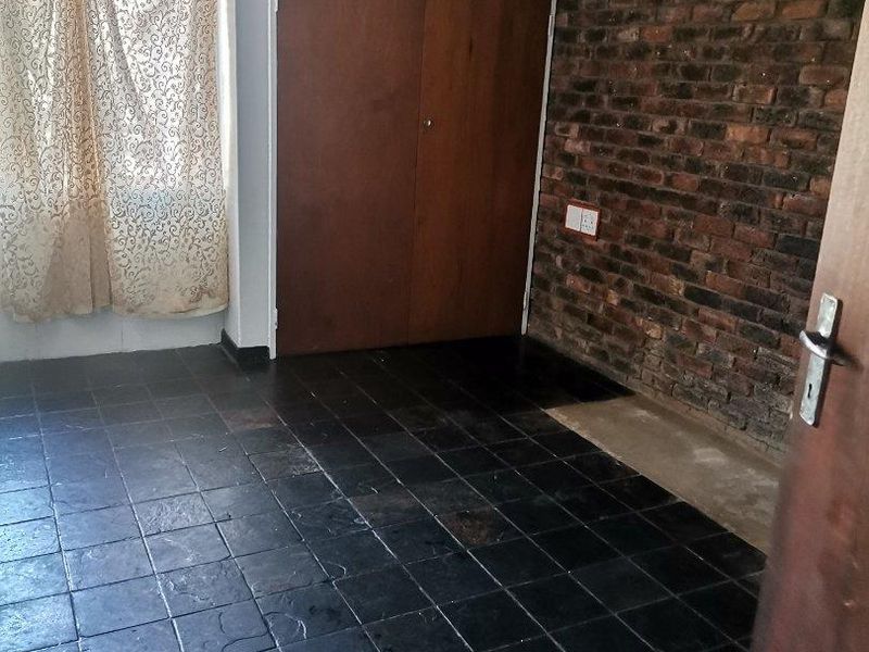 An empty bedroom featuring dark tiled flooring, an exposed brick feature wall, and built-in wooden cupboards.