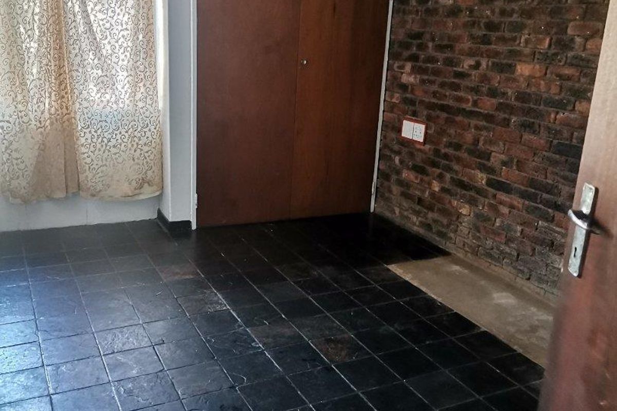 An empty bedroom featuring dark tiled flooring, an exposed brick feature wall, and built-in wooden cupboards.