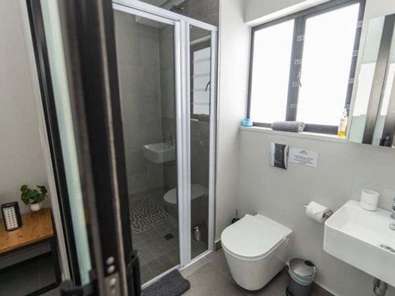 Modern bathroom featuring a wall-mounted toilet, wall-mounted basin, and a glass-enclosed shower with neutral tiling.