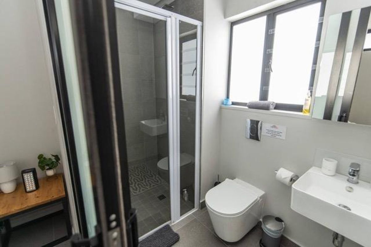 Modern bathroom featuring a wall-mounted toilet, wall-mounted basin, and a glass-enclosed shower with neutral tiling.