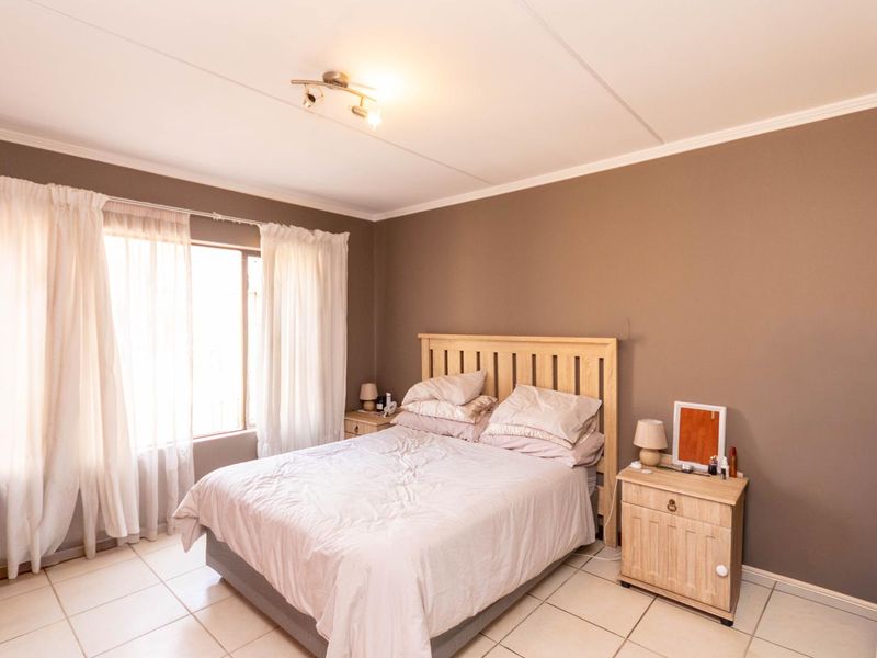 A well-lit bedroom featuring neutral wall tones, tiled flooring, and large windows with curtain rails, providing a comfortable and functional living space.