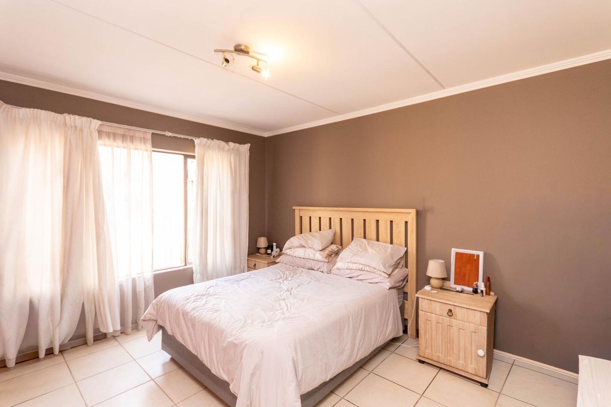 A well-lit bedroom featuring neutral wall tones, tiled flooring, and large windows with curtain rails, providing a comfortable and functional living space.