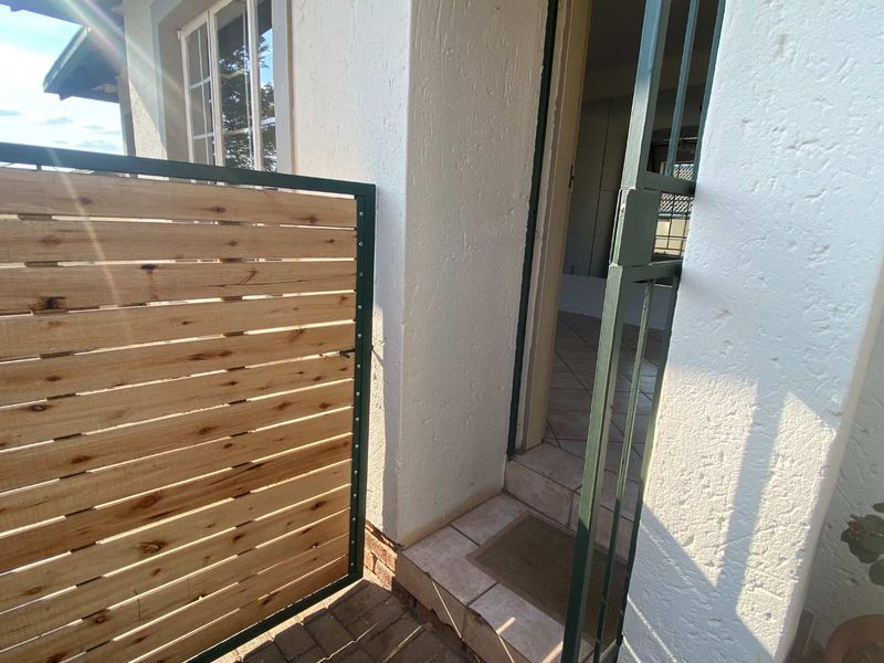 A private entrance area featuring a modern timber slat gate, metal security gate, and tiled threshold leading into the townhouse.