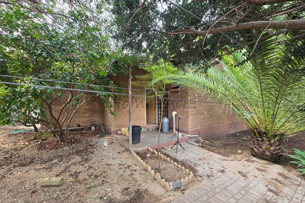 Exterior view of a brick-built structure featuring a covered patio area, surrounded by mature trees and established garden landscaping.