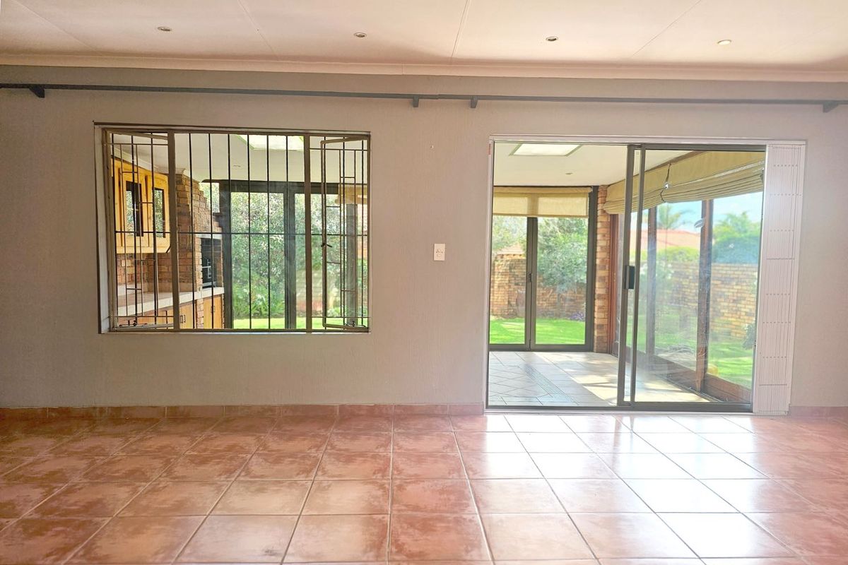 Spacious living area featuring ceramic floor tiles, large sliding glass doors, and security bars, providing direct access to an enclosed patio and garden.