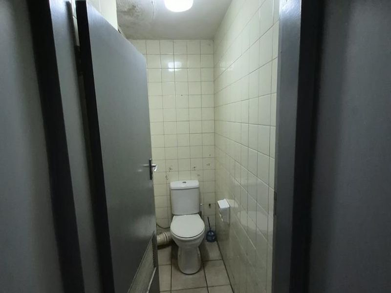 A small, functional guest toilet featuring tiled walls and flooring, showing signs of ceiling water damage requiring maintenance.