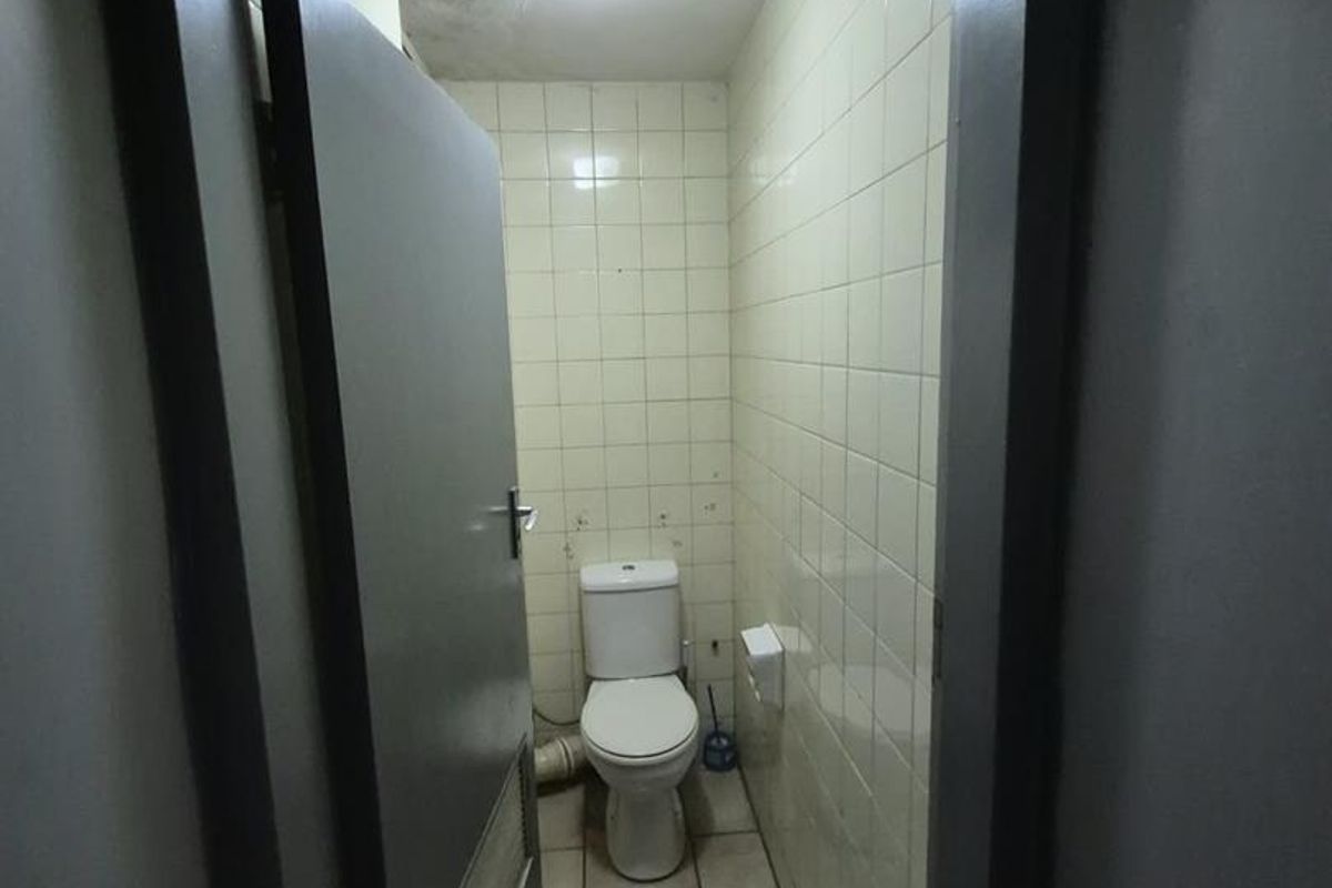 A small, functional guest toilet featuring tiled walls and flooring, showing signs of ceiling water damage requiring maintenance.