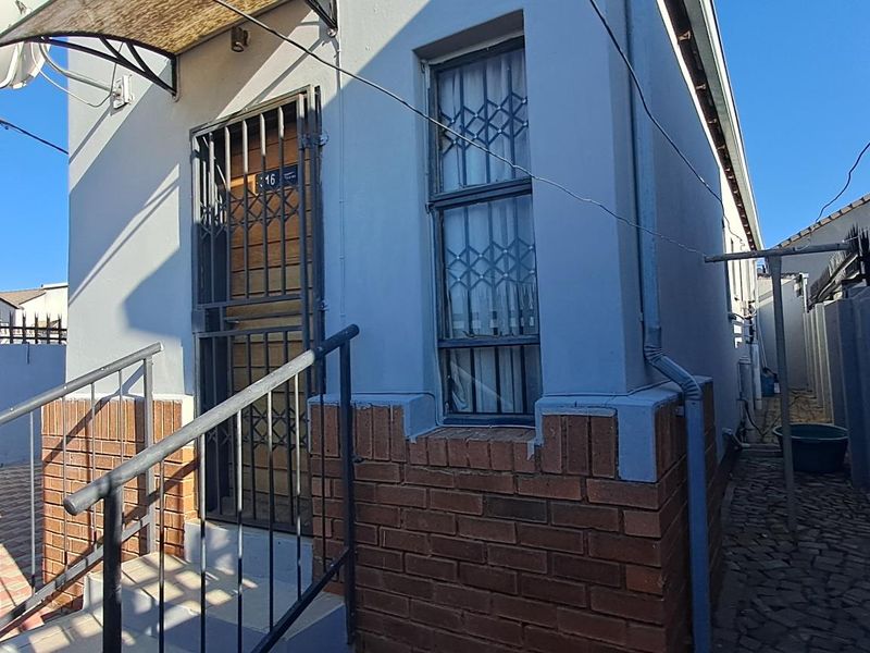 Front entrance of the house featuring a security gate, brick base detailing, and a paved driveway area.