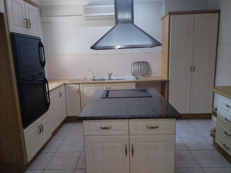 A functional kitchen featuring built-in cabinetry, a central island with a cooktop, granite countertops, and a stainless steel extractor fan.