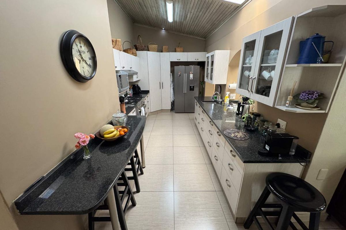 A functional galley-style kitchen featuring granite countertops, ample built-in cabinetry, integrated appliances, and a distinctive sloped timber ceiling.