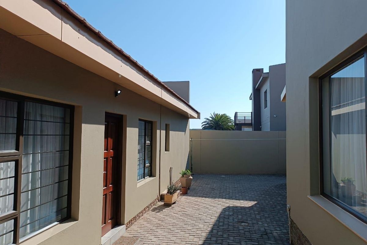 A well-maintained paved side passage or rear courtyard area featuring clean exterior walls, secure window bars, and perimeter boundary walling.