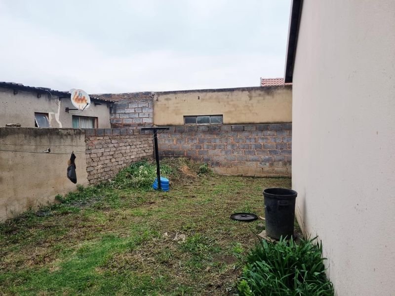 A rear exterior yard area featuring boundary walls and a grassed space, requiring landscaping and maintenance to improve the overall property appeal.