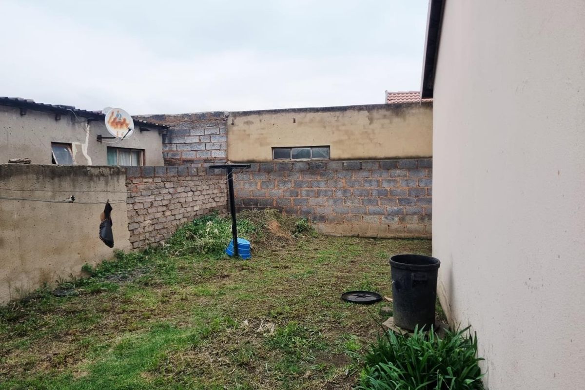 A rear exterior yard area featuring boundary walls and a grassed space, requiring landscaping and maintenance to improve the overall property appeal.