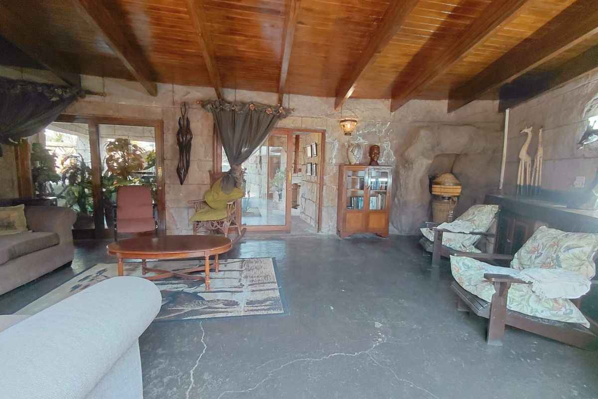 Spacious living area featuring a rustic stone wall, exposed timber beam ceiling, and concrete flooring with access to the outdoor area via sliding glass doors.
