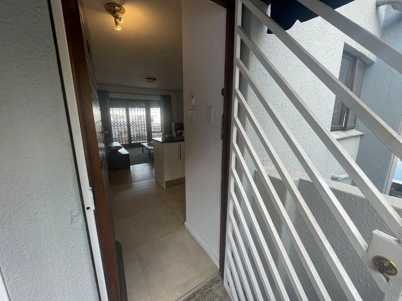 View from the entrance looking into the apartment, featuring a security gate, tiled flooring, and an open-plan layout leading to the living area.