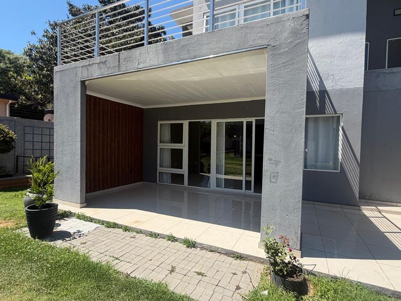 A covered patio area featuring tiled flooring, wood-look wall accents, and sliding glass doors, with an upper balcony enclosed by a stainless steel railing.