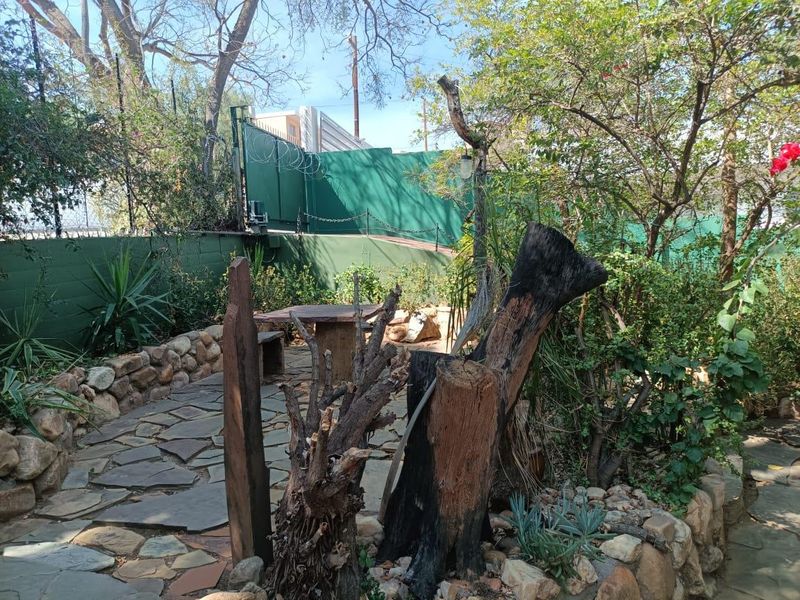 A rustic garden area featuring stone paving, natural stone retaining walls, and perimeter fencing with security wire, requiring landscaping maintenance.