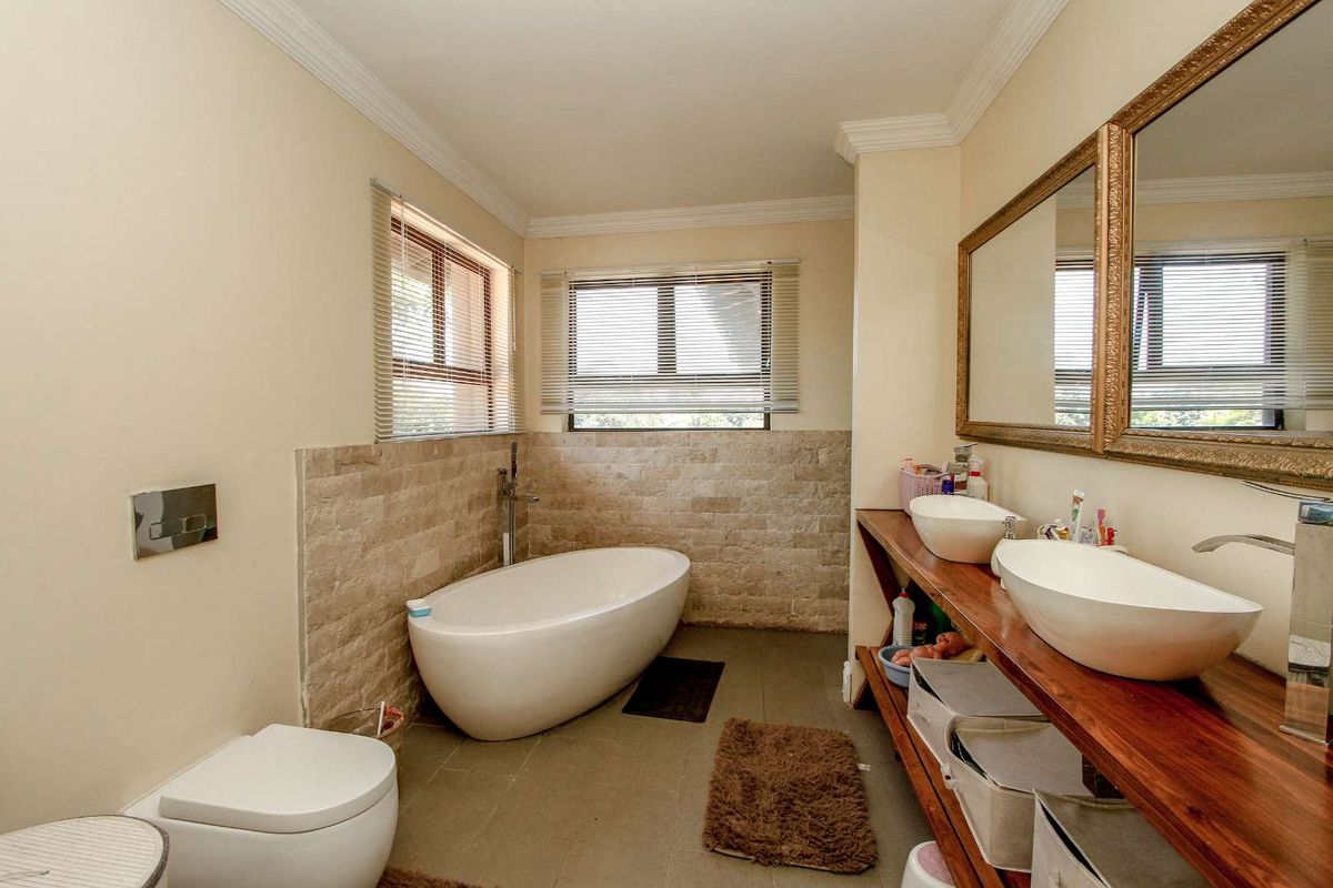 A well-appointed bathroom featuring a freestanding bathtub, dual vessel sinks on a wooden vanity, and stone-tiled wall accents.