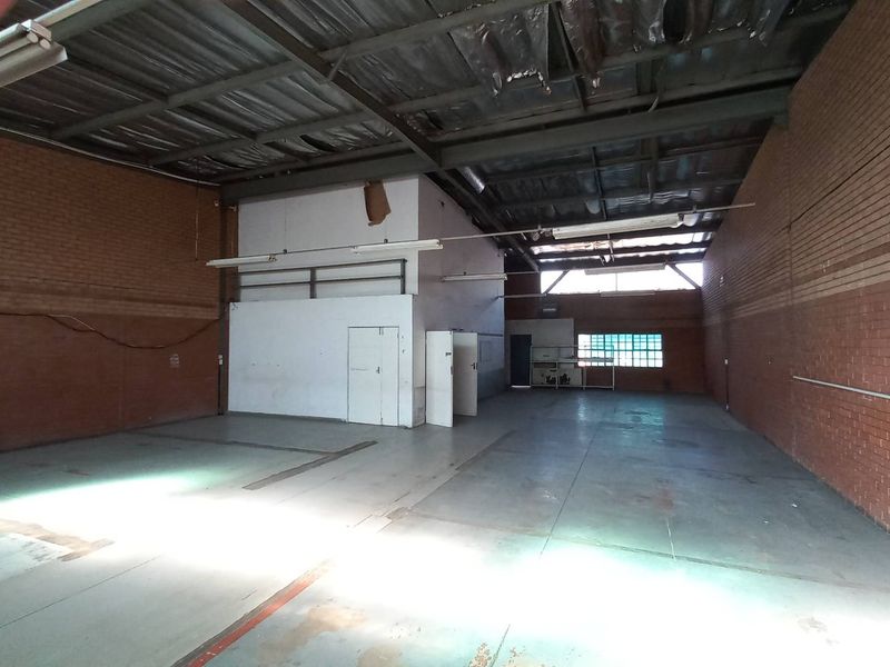 Spacious industrial warehouse unit featuring exposed brick walls, high-clearance steel roof structure, and concrete flooring, suitable for storage or light manufacturing operations.