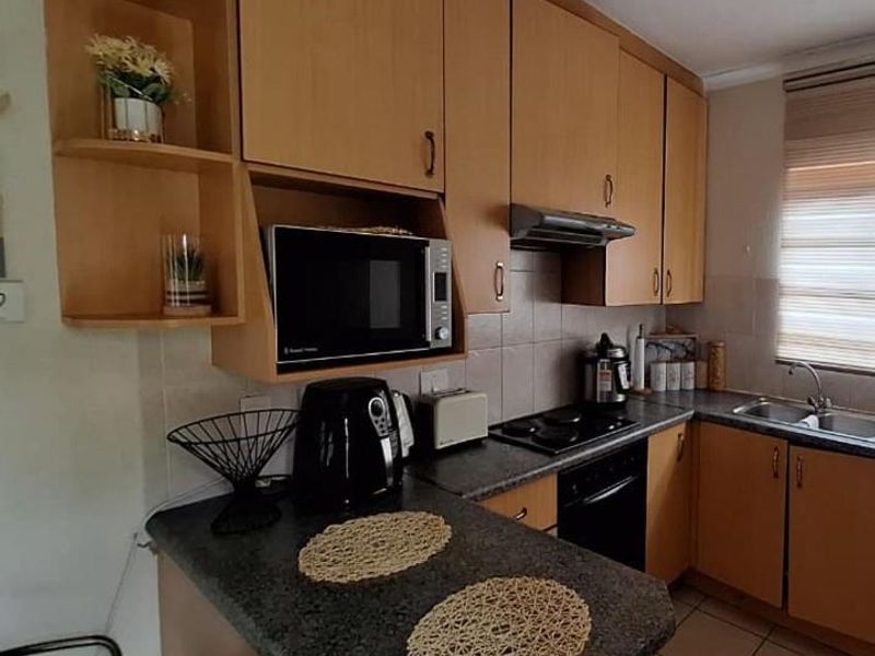 Functional kitchen featuring wood-tone cabinetry, dark laminate countertops, built-in oven and hob, and a tiled backsplash with a window blind.