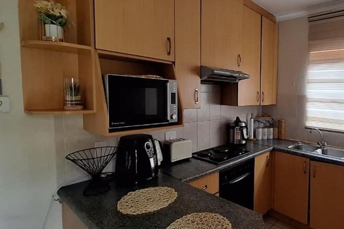 Functional kitchen featuring wood-tone cabinetry, dark laminate countertops, built-in oven and hob, and a tiled backsplash with a window blind.