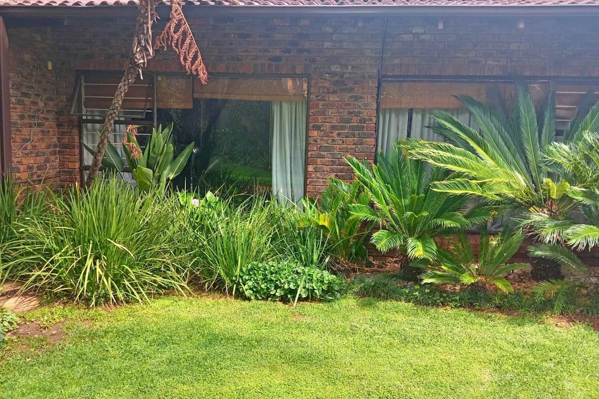 Rear view of the house featuring a classic face-brick facade, large windows, and a well-established garden with mature landscaping.