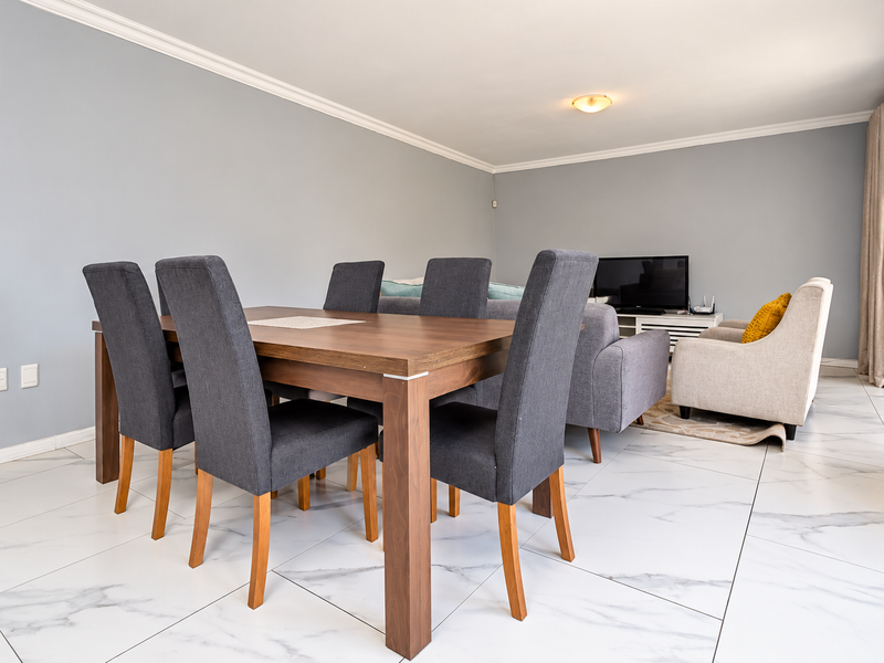 A bright open-plan living and dining area featuring modern marble-look floor tiles, crown molding, and direct access to an outdoor space via sliding doors.