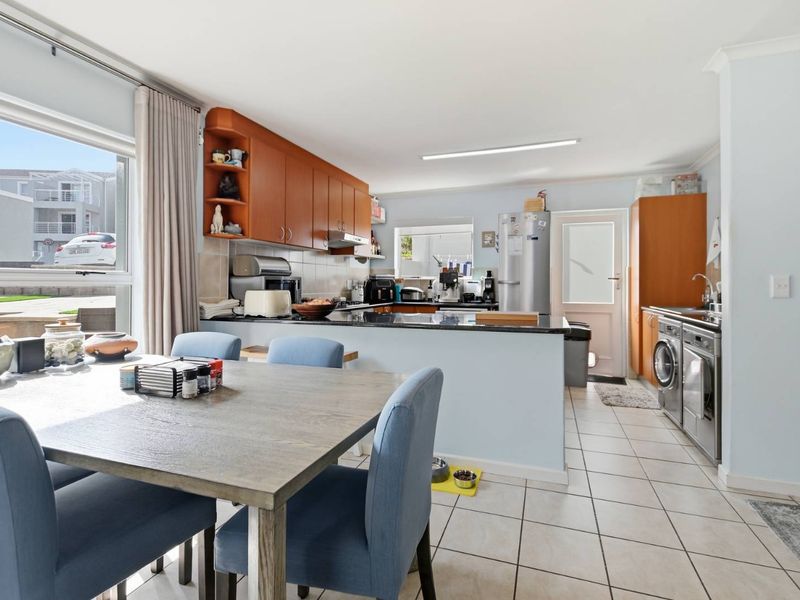 Open-plan kitchen and dining area featuring wooden cabinetry, granite countertops, tiled flooring, and integrated laundry facilities with direct access to the exterior.