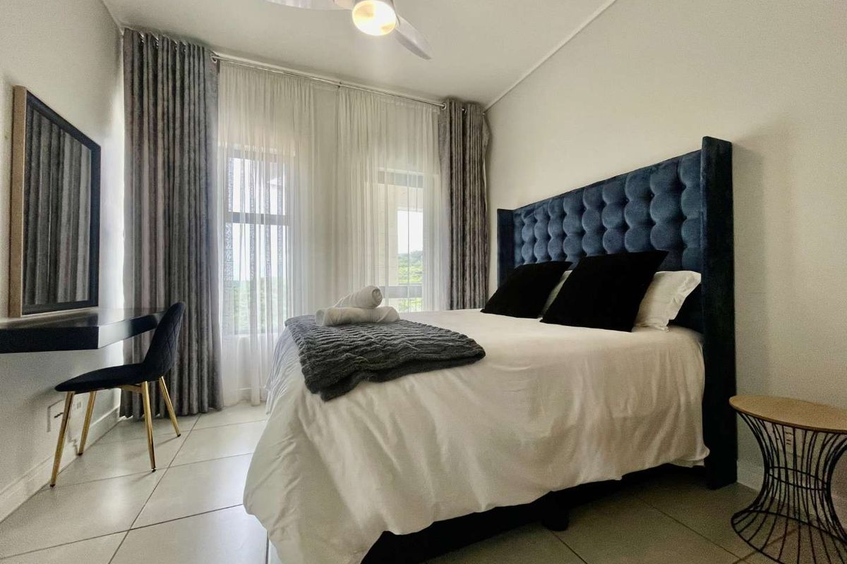 A well-maintained bedroom featuring tiled flooring, a ceiling fan, and large windows with floor-to-ceiling curtains, providing a bright and comfortable living space.
