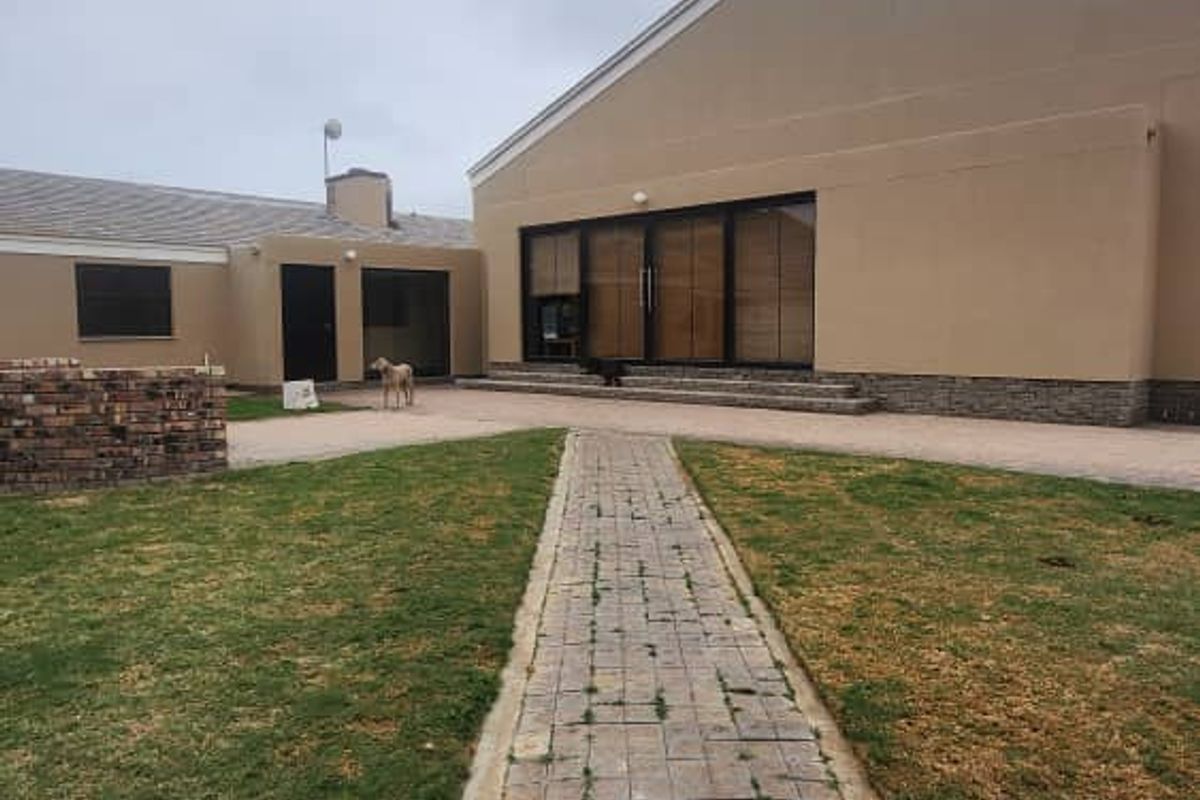 Rear view of the property featuring a paved walkway leading to a large sliding glass door entrance and a landscaped garden area.