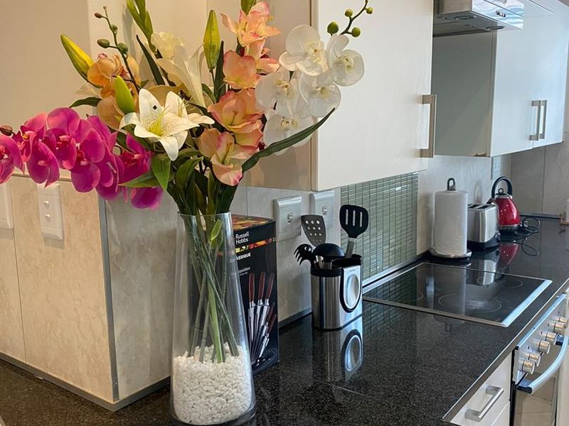 A modern kitchen featuring dark granite countertops, a glass mosaic backsplash, and integrated stainless steel appliances including an oven and extractor fan.