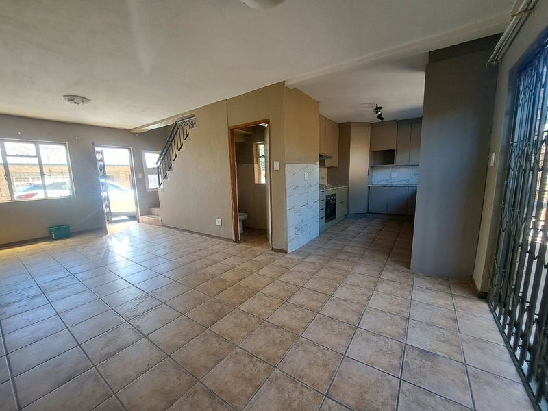 Open-plan living area featuring tiled floors, a functional kitchen with built-in appliances, and a staircase leading to the upper level.