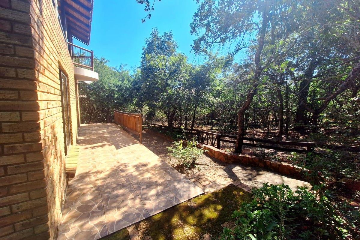 A rear patio area featuring tiled flooring, a wooden balustrade, and direct access to a wooded garden setting.