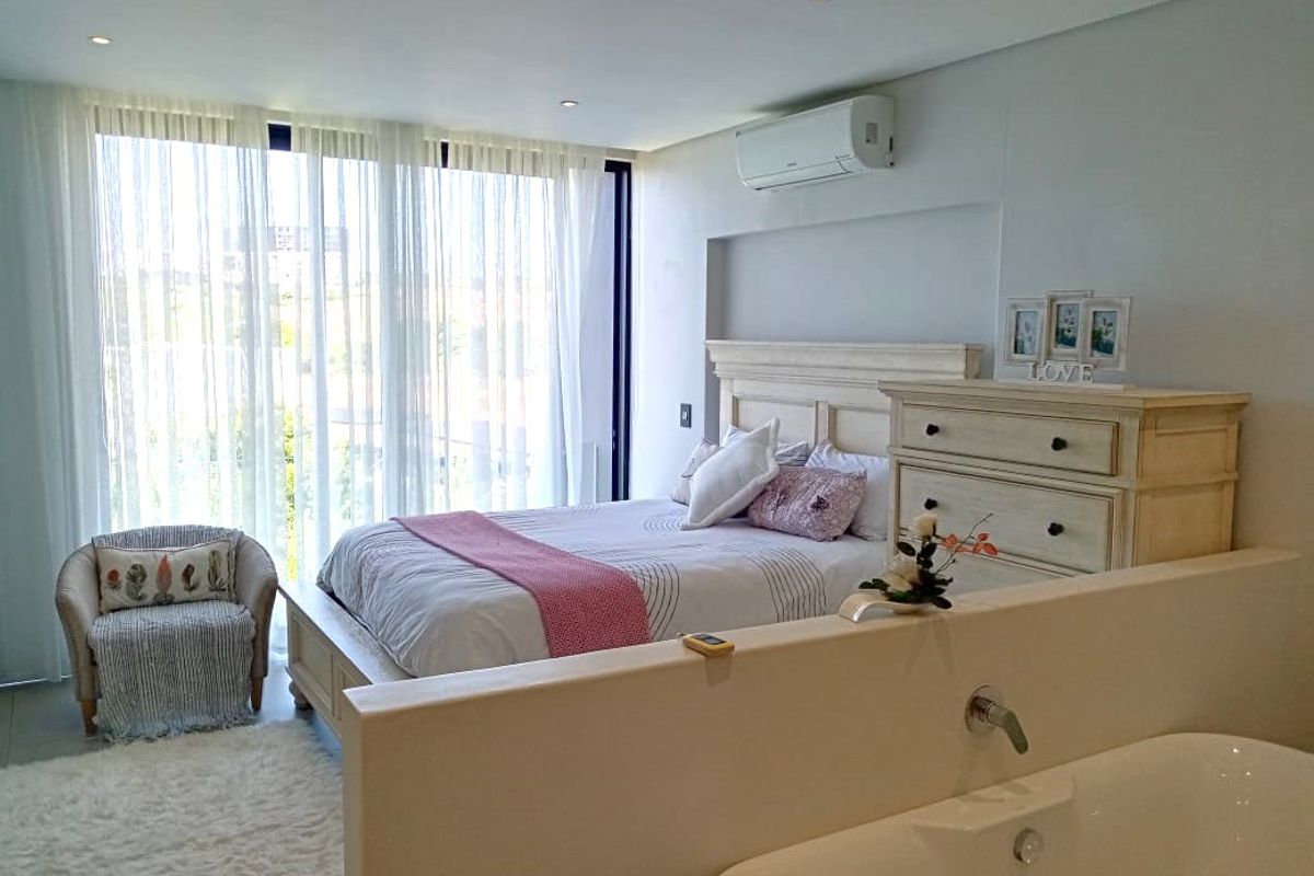 Spacious bedroom featuring an open-plan layout with an integrated ensuite bathtub, split-system air conditioning, and large sliding doors leading to a balcony.