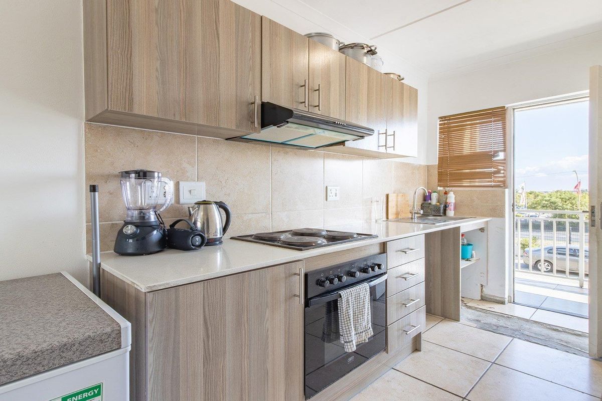 Functional kitchen featuring wood-look laminate cabinetry, stone countertops, built-in oven, hob, and direct access to a balcony area.