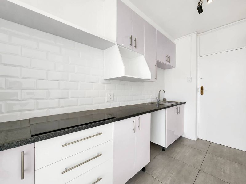 A clean, modern kitchen featuring white cabinetry, a black granite countertop, subway tile backsplash, and integrated hob with stainless steel sink.