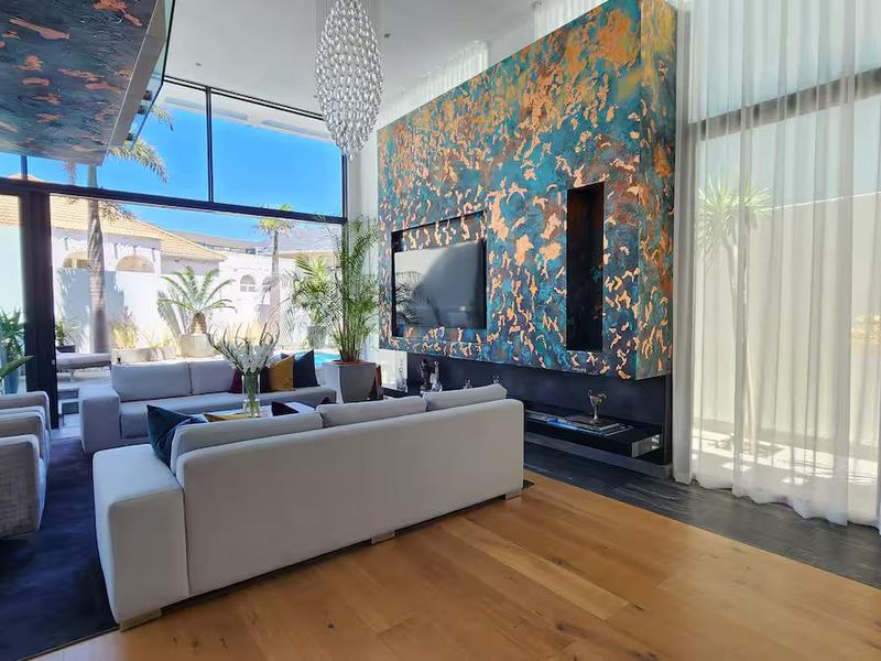 Spacious living room featuring high ceilings, hardwood flooring, floor-to-ceiling windows, and a striking decorative feature wall with a built-in fireplace.