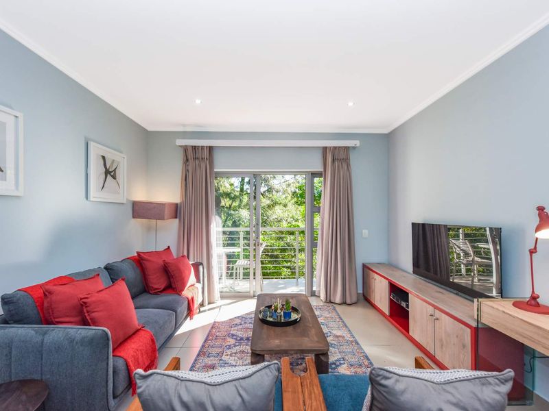 A bright and well-maintained living room featuring tiled flooring, recessed lighting, and a sliding glass door that opens onto a balcony with greenery views.